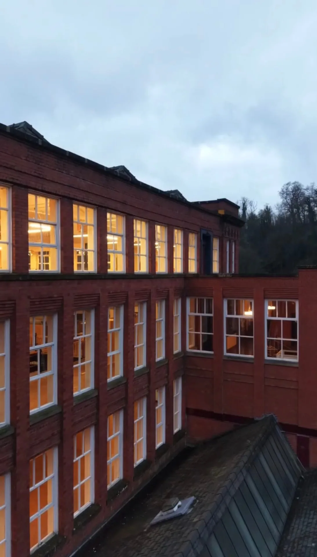 Warmly lit windows in the brick façade of Masson Mills at dusk